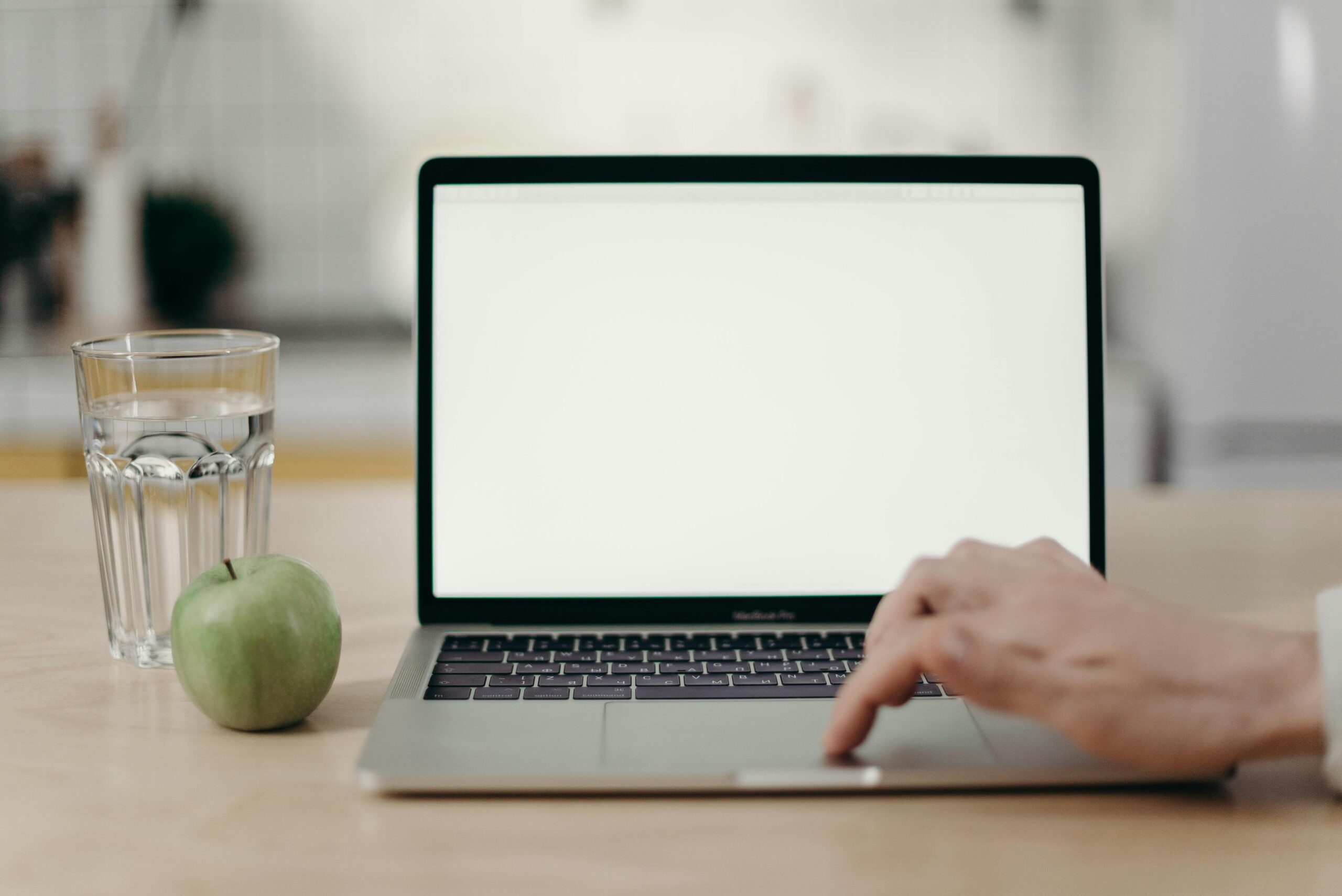 Minimalist home office scene featuring blank laptop screen, green apple, and glass of water.